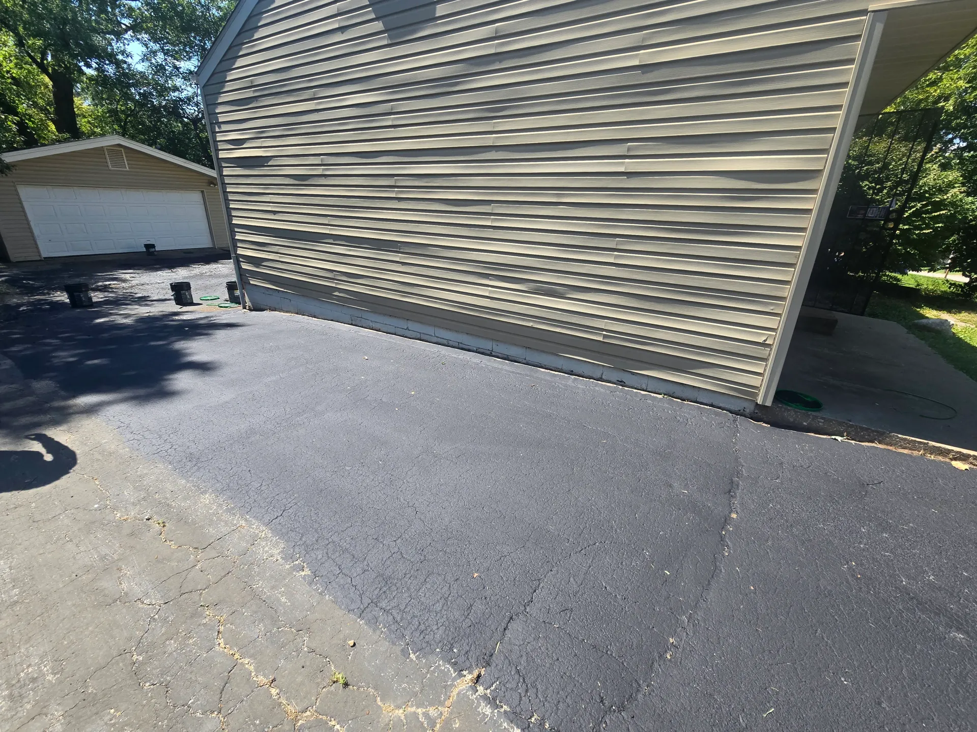 Residential driveway mid-sealcoating near a garage with a fresh dark finish.
