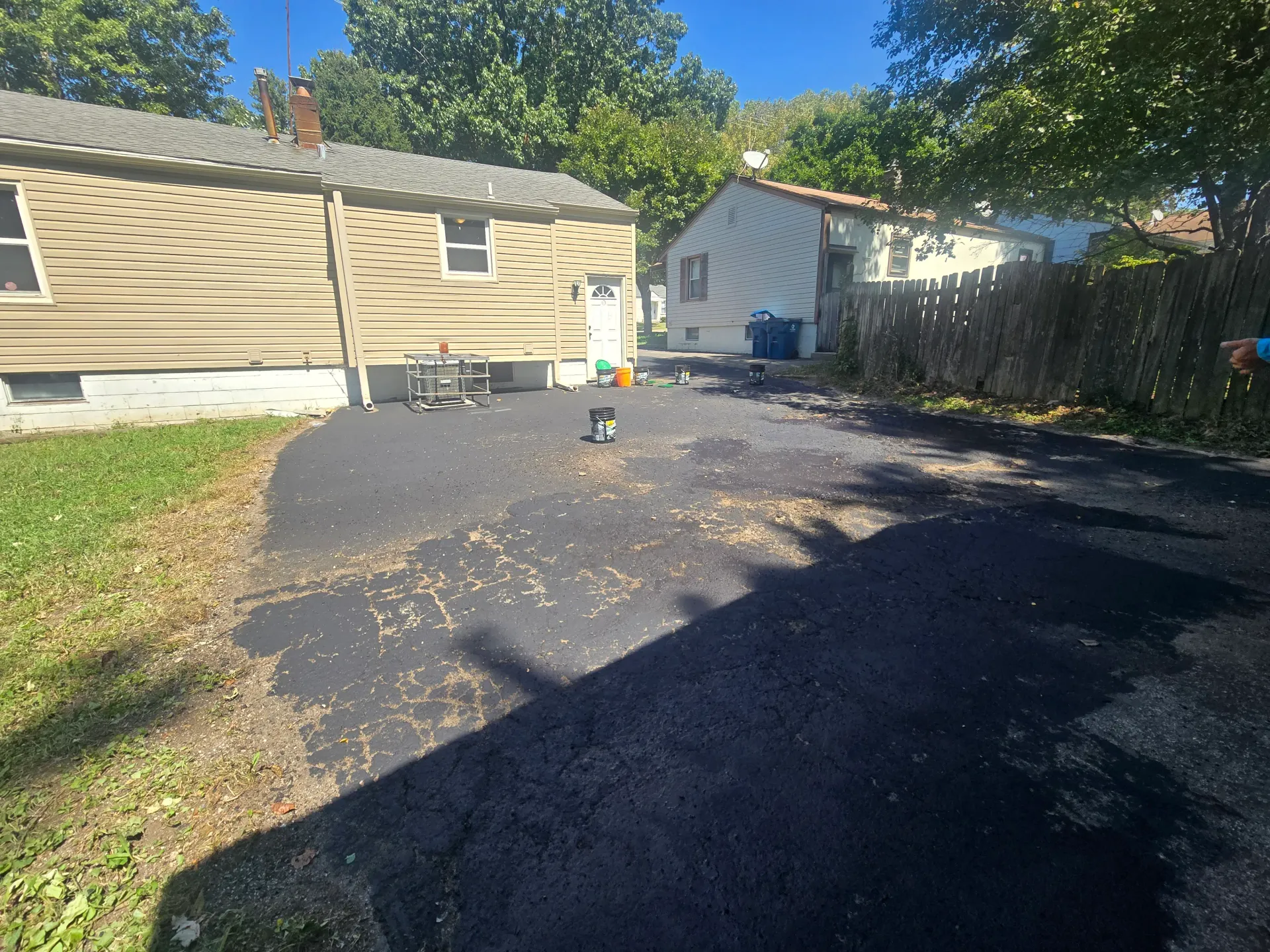 Driveway partially finished with fresh black sealant and buckets nearby.