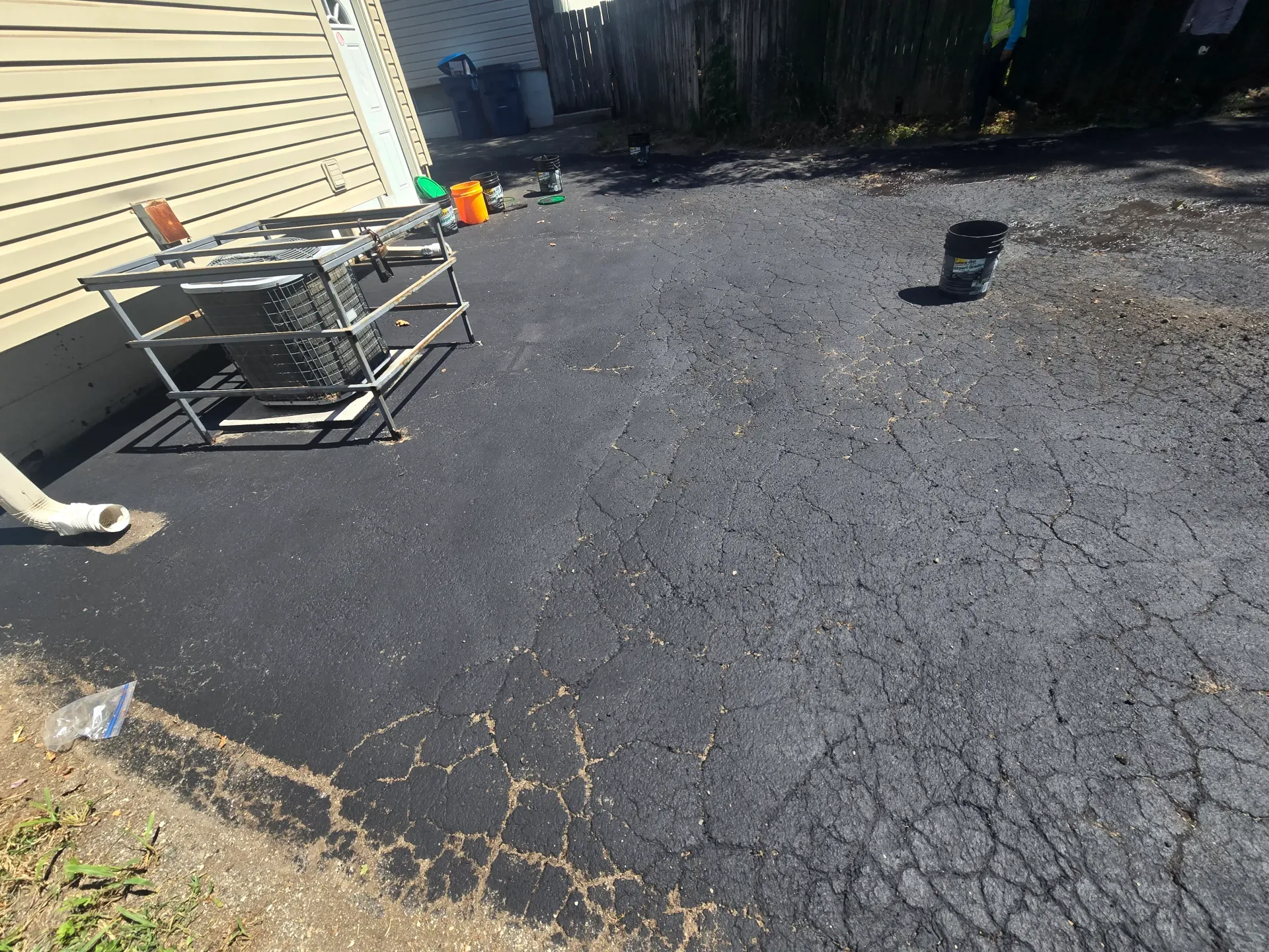 Sealcoating in progress over cracked asphalt with buckets staged near the foundation.