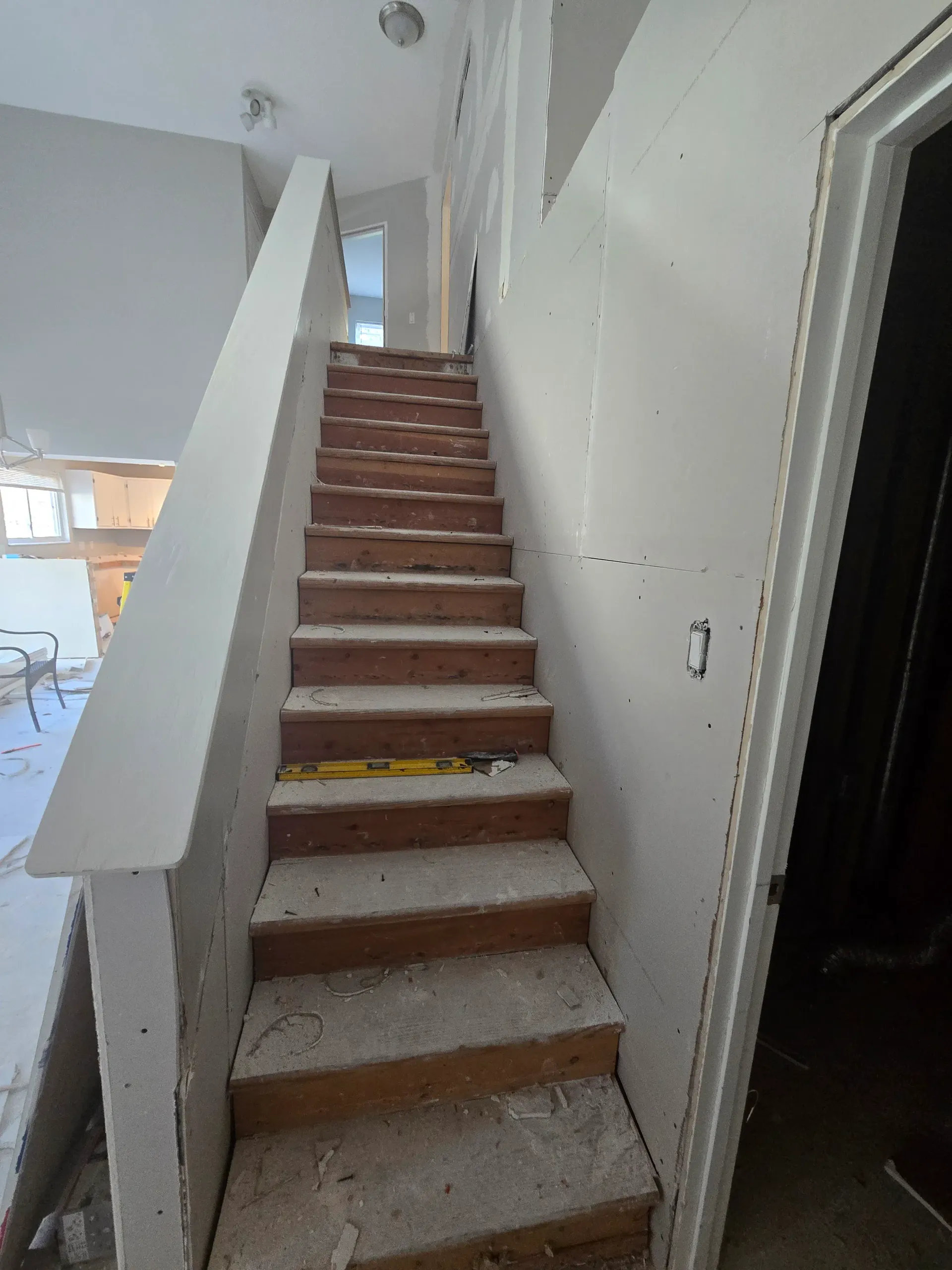 Interior staircase renovation with exposed treads, new drywall, and a level on a step.